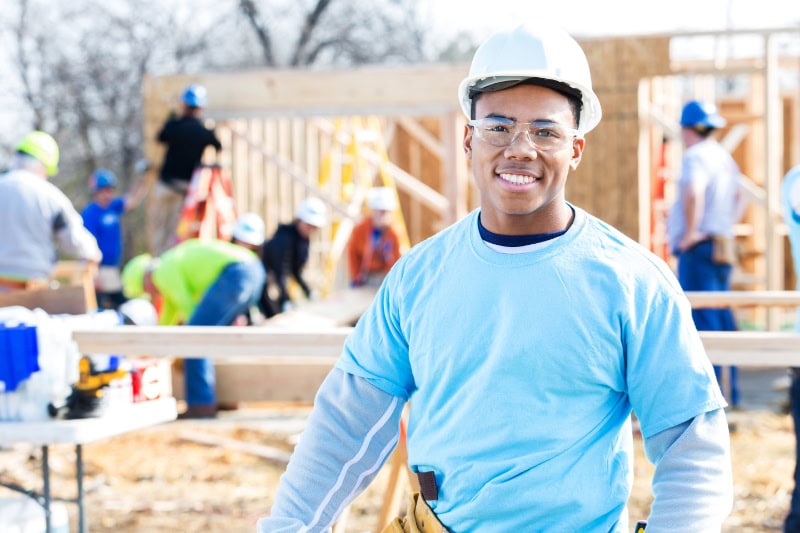 Schedule Your Annual Furnace Inspection Now. Photo of a construction worker smiling with workers in the background.
