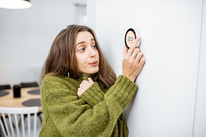 woman turning up her heat in a sweater.